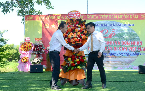 Two men holding flowers in front of a signDescription automatically generated